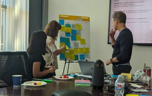 Photo of 3 people looking at a board of sticky notes