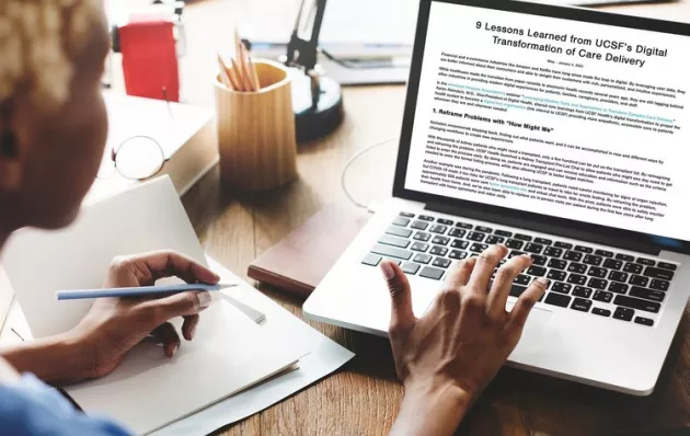 Photo of a person typing on a laptop and taking notes