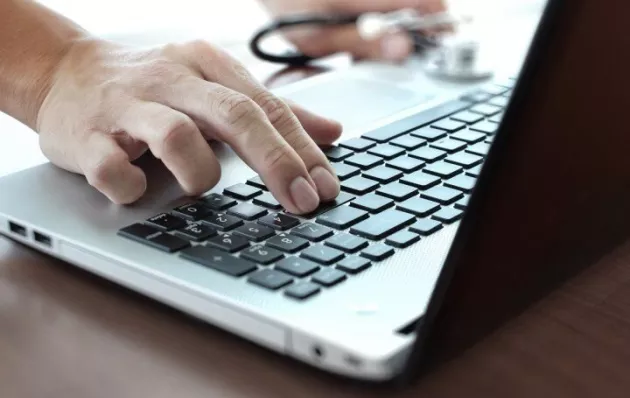 Close up view of a doctor's hand typing out notes on a laptop