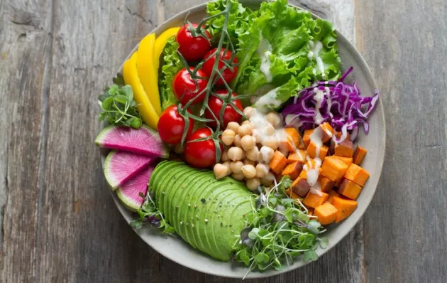 Bowl of healthy snacking options such as lettuce, carrot, chick peas, sprouts, avocado slices, tomatoes, and peppers.